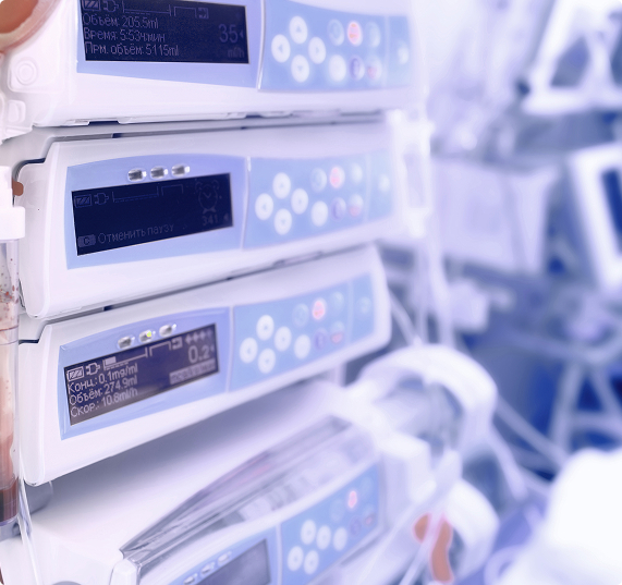 Stack of medical infusion pumps in a clinical setting — white and light blue tones, digital screens with buttons.